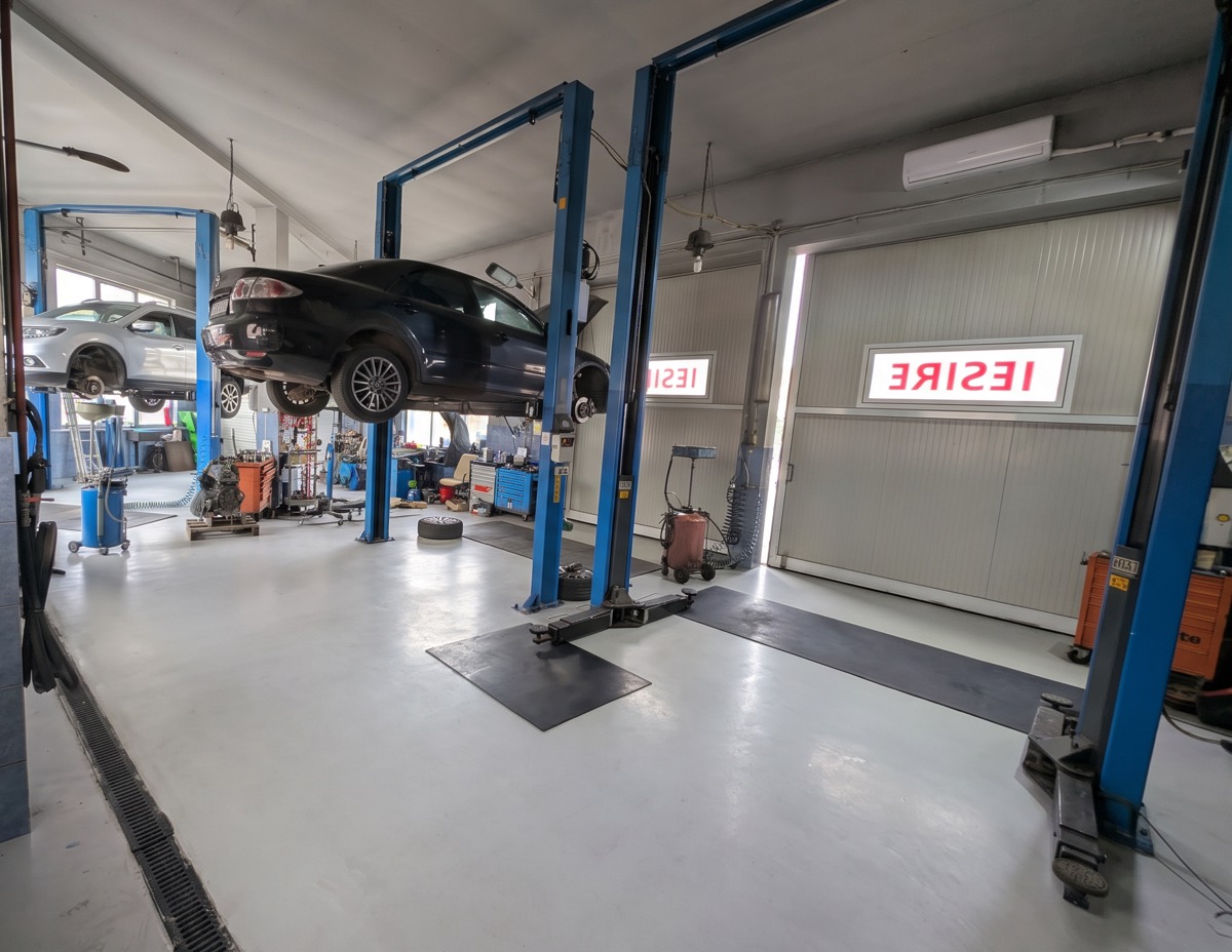 Innenansicht der autoFYG-Werkstatt: zwei Fahrzeuge auf Hebebühnen, sauberer grauer Boden und die Ausfahrtstore
